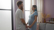 © Krakenimages.com - Pregnant woman and bearded man holding hands and smiling in a brightly lit living room, showcasing love and anticipation in a cozy, modern home setting.