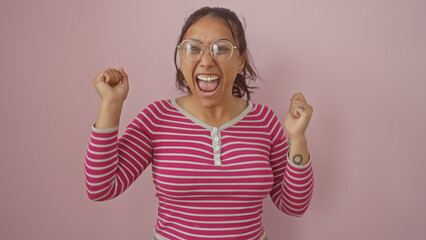 Poster - A joyful woman in a striped shirt cheers with a raised fist against a pink background, showcasing positive energy and excitement.