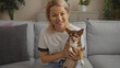© Krakenimages.com - A young blonde caucasian woman sitting in an indoor living room, smiling and holding her chihuahua dog.