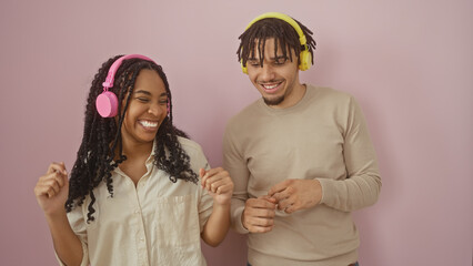 A smiling man and woman enjoy music together against a pink background.