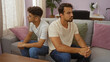 © Krakenimages.com - Father and son sitting together in a living room looking contemplative, showcasing family bond indoors with a hispanic background and casual setting