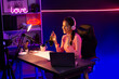 © Summit Art Creations - Smiling creative young beautiful Asian influencer talking in channel with positive podcast speech at night time, using laptop for presentation online at pink neon light modern studio. Stratagem.