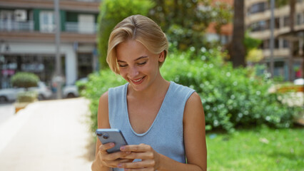 Sticker - Young woman with short blonde hair using a smartphone outside in an urban park on a sunny day