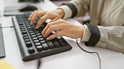 A mature woman's hands typing on a keyboard in a modern office setting.