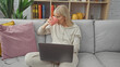© Krakenimages.com - Caucasian woman drinking coffee while working on a laptop in a cozy living room environment.