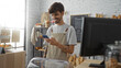 © Krakenimages.com - Young hispanic man with a beard smiling while using a smartphone in a bakery shop interior with shelves of bread and pastries around