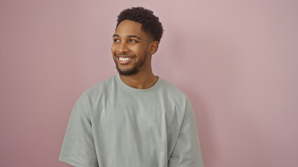 Smiling african american man standing against a pink wall dressed in casual attire.