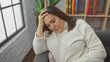 © Krakenimages.com - Middle-aged woman feeling stressed in a comfortable home living room, touching her forehead in a gesture of worry or headache.