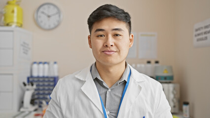 A young asian man in a white lab coat stands confidently in a medical laboratory environment, embodying professionalism and expertise.