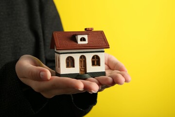 Wall Mural - Woman with house model on yellow background, closeup