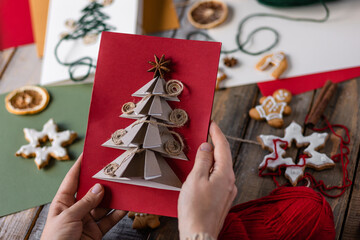 Wall Mural - Handmade New Year origami postcard with paper christmas fir tree. Holiday idea for family time and gift for beloved. Gingerbread cookies, lights, wooden background. Zero waste, recyclable materials