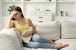 © New Africa - Woman using hot water bottle to relieve menstrual pain on sofa at home
