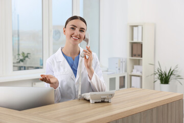 Sticker - Professional receptionist talking on phone at wooden desk in hospital