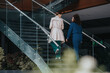 © qunica.com - Two businesspeople walking upstairs in a modern office building, engaging in a work discussion. Professional setting and corporate environment.