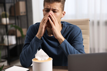 Wall Mural - Young man with tissue suffering from sinusitis at wooden table indoors