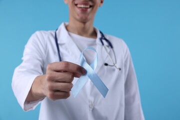 Sticker - Prostate cancer awareness. Doctor holding light blue ribbon as symbol of support on color background, selective focus