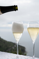 Pouring of cold sparkling wine, cava or champagne in two glasses on table with sea water view