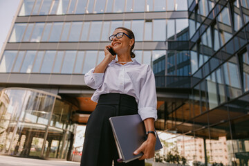 A businesswoman is engaged in a phone conversation while standing outside a modern office building