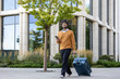 © Liubomir - Smiling man in casual clothes walking with suitcase and phone outside modern office building. Image conveys concepts of travel, business, connectivity, and urban lifestyle.