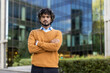 © Liubomir - Confident young man with curly hair standing with arms crossed in front of modern glass building. Urban setting suggesting professional atmosphere and modern lifestyle.