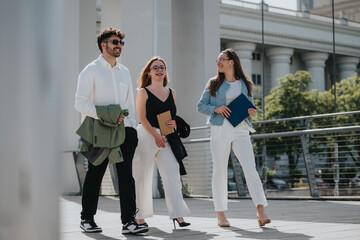 Three smiling business colleagues walking outdoors, enjoying a sunny day. They look happy, engaged, and professional.