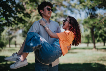 Wall Mural - A joyful couple shares a playful moment in a park. The man lifts the woman, both smiling and wearing sunglasses, enjoying a sunny day together.