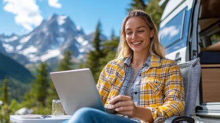 Wall Mural - A smiling woman in a plaid shirt using her laptop outdoors near a camper van with a stunning mountain view, representing the freedom and flexibility of remote work.