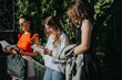 © qunica.com - Three businesswomen participating in an outdoor meeting. They are engaged in a discussion, examining notes and documents. The sunny weather adds a lively atmosphere.