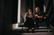 © qunica.com - Two colleagues engaged in a focused business meeting outdoors at night, discussing work while sitting on a staircase.