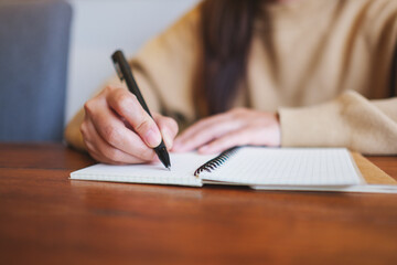 Wall Mural - Closeup image of a woman writing on a notebook on wooden table