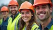 © umut hasanoglu - Smiling construction workers wearing orange helmets and safety vests at a construction site.