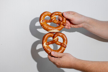 Hands holding two traditional pretzels, ideal for illustrating German cuisine or Oktoberfest celebrations