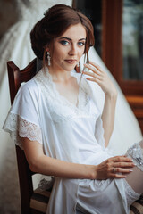 A woman is sitting on a chair wearing a white dress. She is smiling and looking at the camera