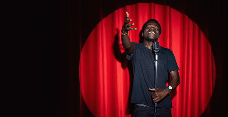 Wall Mural - African, american man comic in costume performing standup monologue on stage with red curtains. Concept comedian show banner