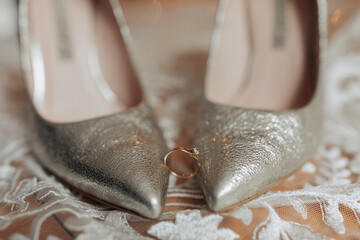 A pair of high heels with a ring on the toe. The shoes are silver and the ring is gold. Concept of elegance and sophistication, as the shoes and ring are both classic and timeless