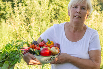 Poster - elderly woman in the garden with fresh vegetables in a bowl. Selective focus