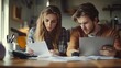 © The Little Hut - Young married couple with many debts doing paperwork together reviewing their bills planning family budget and calculating finances at kitchen table with papers calculator and laptop c : Generative AI