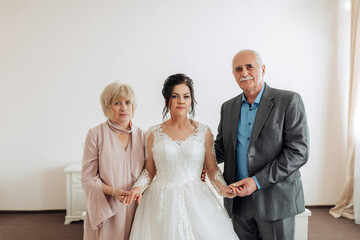 A woman in a wedding dress is standing between two older women. Scene is warm and loving, as the three of them are embracing each other