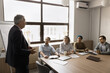 © fizkes - Mature businessman in suit hold formal meeting with stakeholders met in modern boardroom, introduce new corporate goals or project details, share opinion, strategy and plan, leading briefing for staff