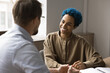 © fizkes - Attractive African blue-haired woman engaged in conversation with male colleague. Professional and friendly business interaction for exchanging ideas, feedback, or updates between teammates in office