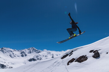 Young female skier jumping from ski jump on sunny day in snowy alpine mountains, moment in flight