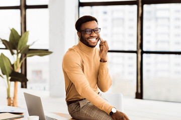 Poster - Work Call. Happy african american manager talking on cell phone, sitting on desk. Free space