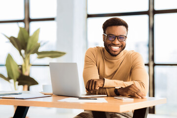 Poster - Blogger At Work. Smiling black man looking at camera, sitting at desk with laptop. Selective focus