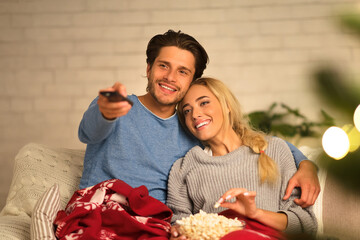 Wall Mural - Loving couple watching tv at Christmas eve and eating popcorn at home