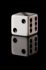 a white six-sided D6 dice with black dots, showing two dots, on a black background with a reflection