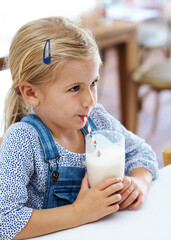 Girl, child and drinking milk in home, nutrition and vitamin d liquid for growth development. Female person, kid and glass of mineral juice for calcium at kitchen table, dairy breakfast and health