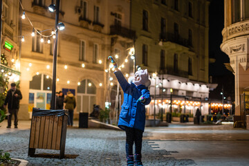 Wall Mural - Little girl, iluminated with street lights. Christmas decoration is in the background