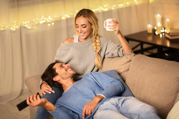 Wall Mural - Loving couple drinking tea and enjoying winter holidays, talking and watching tv on sofa