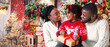 © Prostock-studio - Little afro girl opening Christmas gift box with her parents, bonding together in decorated living room.