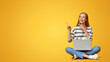 © Prostock-studio - Cheerful Teenage Girl Sitting With Laptop On Her Laps And Pointing At Copy Space On Yellow Background, Panorama